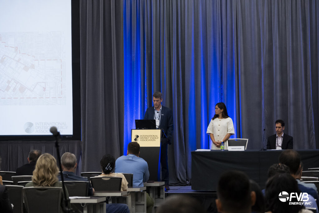Speaker presenting at IDEA2026 in front of a presentation slide, with panelists seated on stage and attendees in the audience.