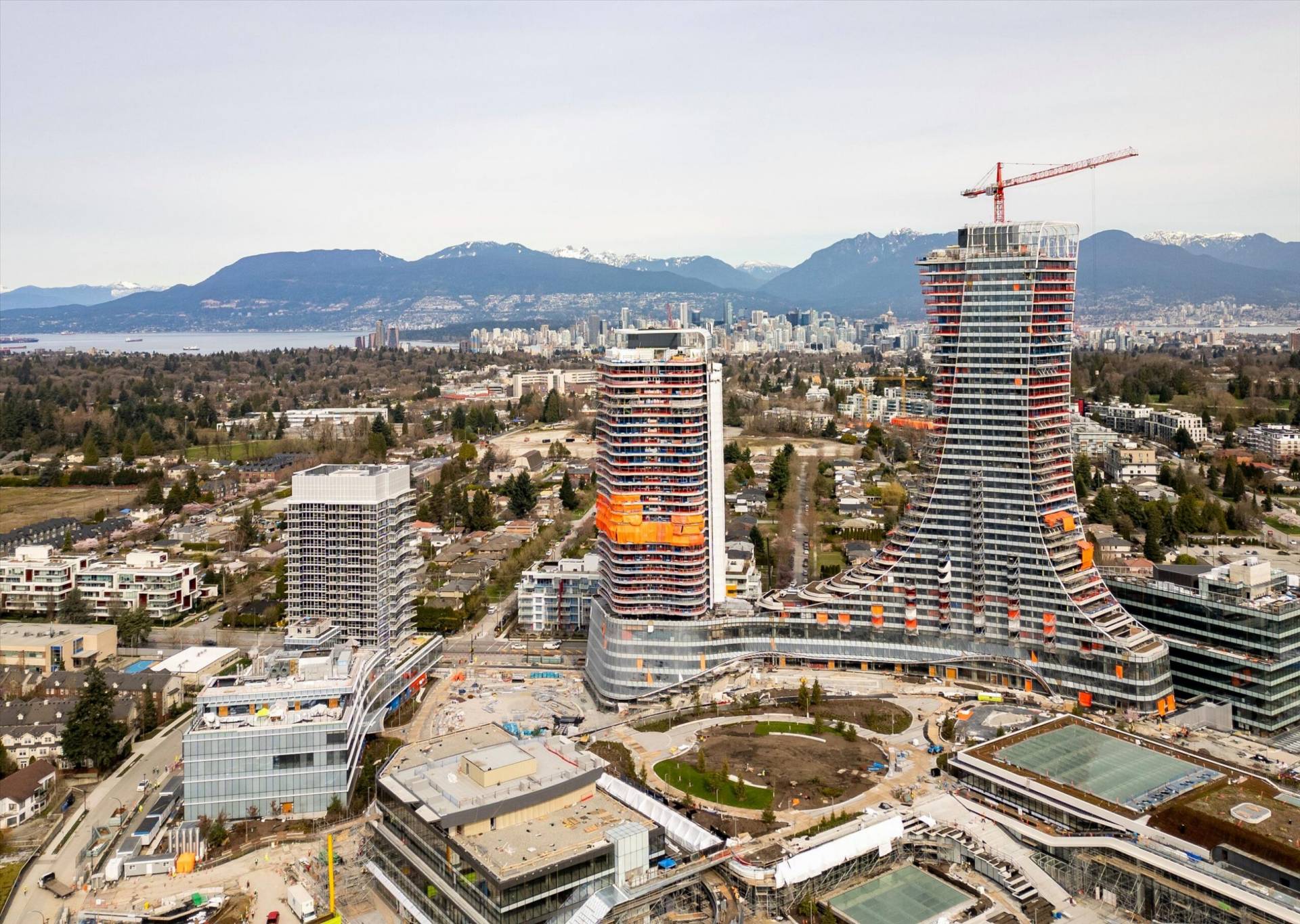 Aerial view of the Oakridge Centre Redevelopment showing high‑rise towers under construction, cranes, and surrounding neighbourhood with mountains in the background.